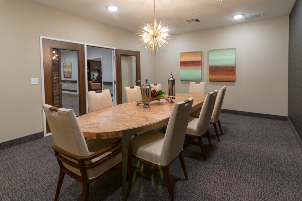 A modern dining or conference room with a large wooden table, beige upholstered chairs, and contemporary artwork on the walls.