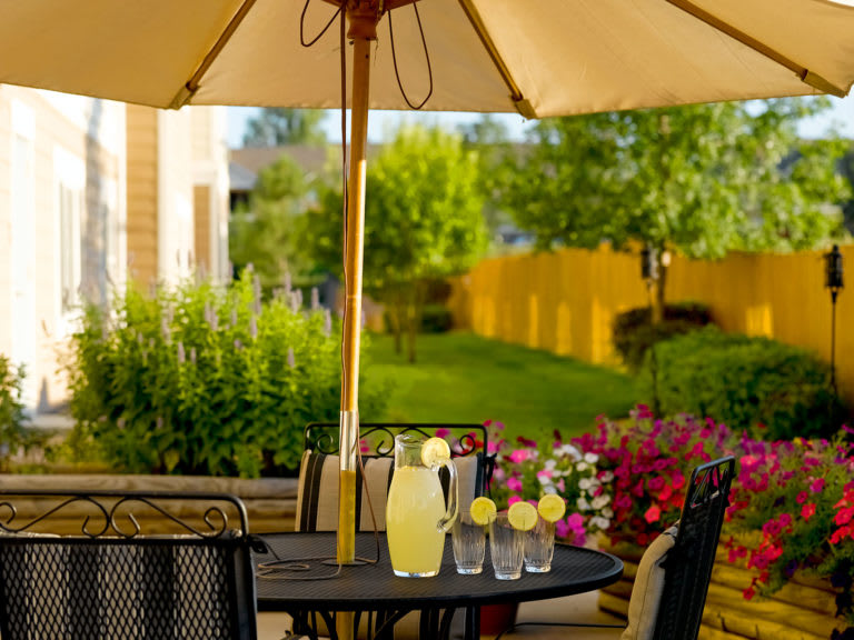 A sunny patio setup with a table under an umbrella, featuring a pitcher of lemonade and glasses ready for a refreshing drink.