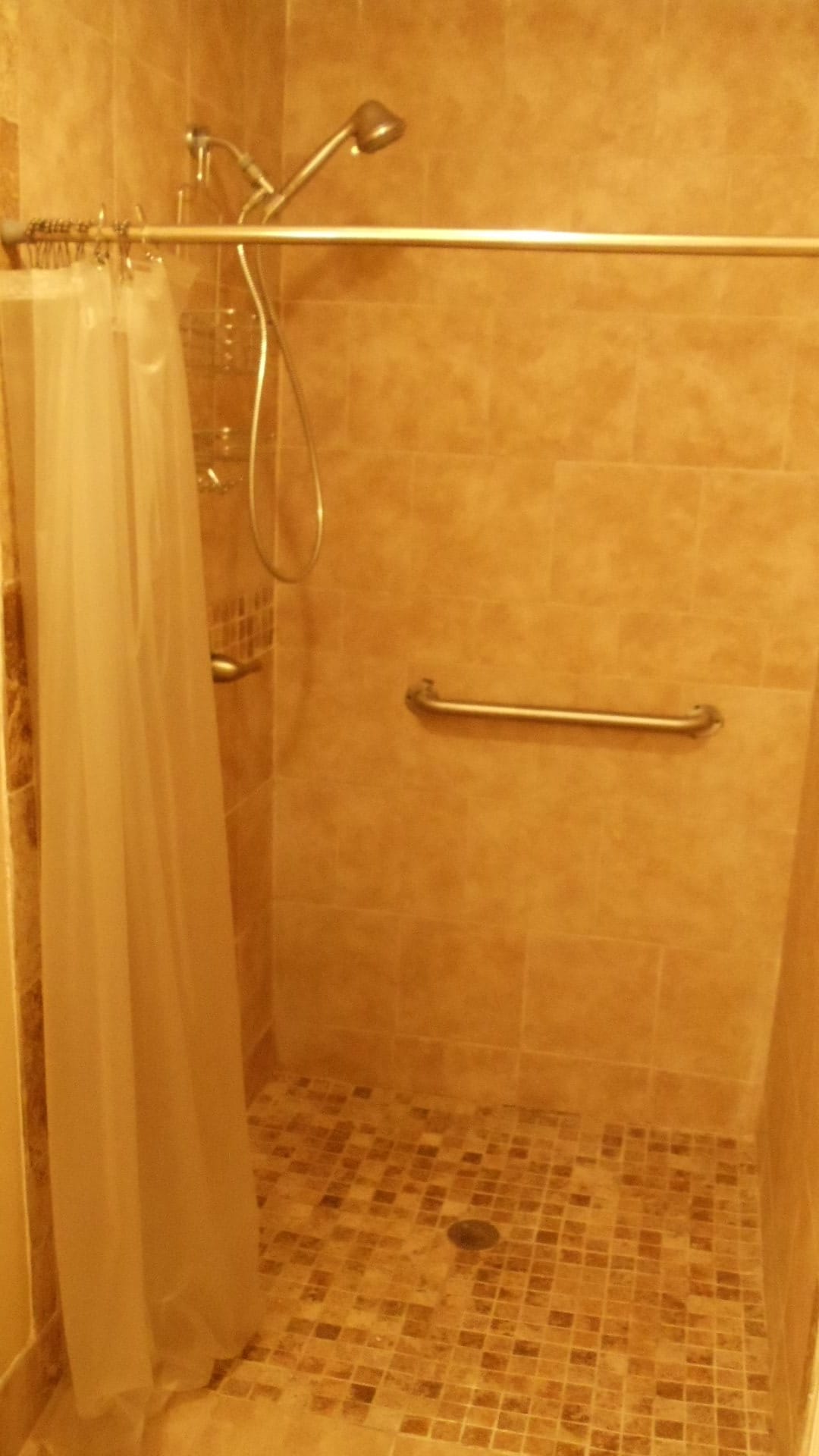 A tiled shower area with a curtain and a grab bar.