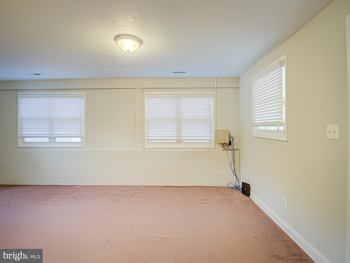 An empty room with three windows featuring blinds and a ceiling light fixture.