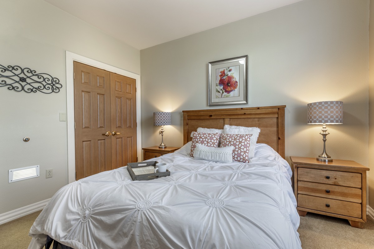 A cozy bedroom featuring a neatly made bed with white bedding, flanked by wooden nightstands and modern lamps.