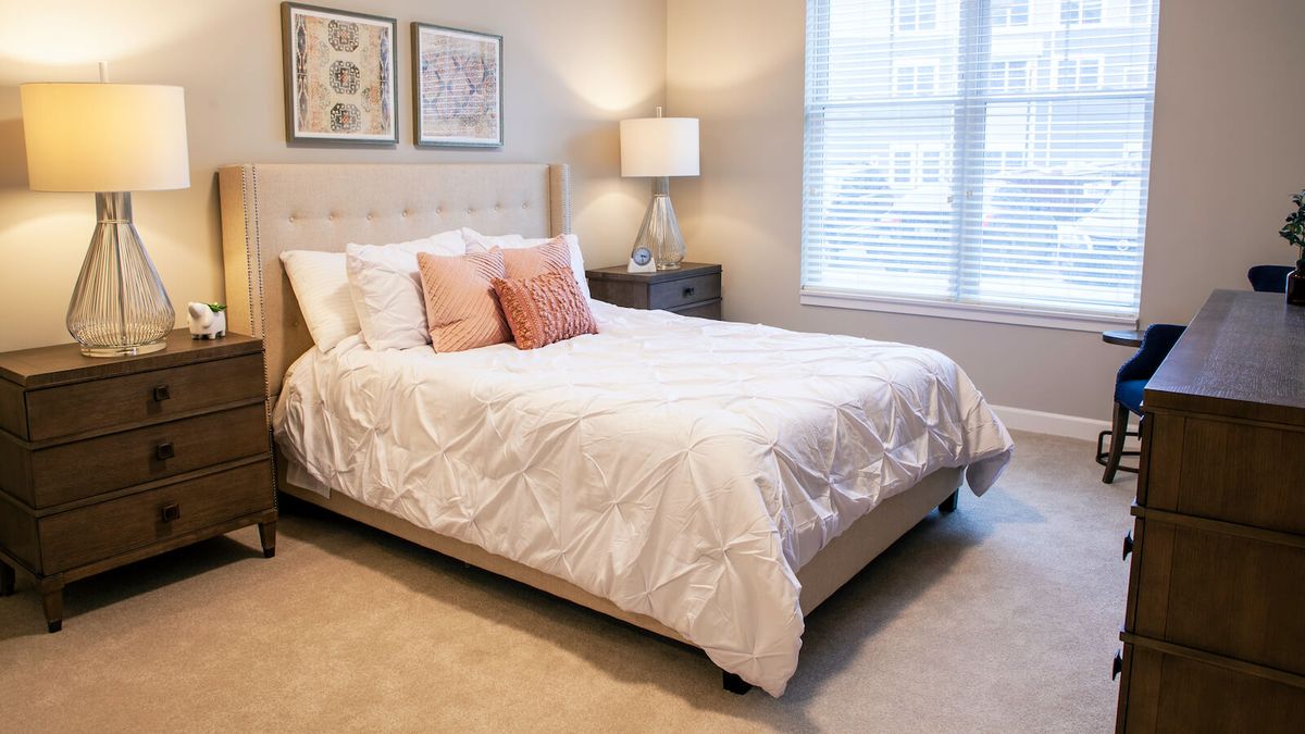 A cozy bedroom with a neatly made bed, decorative pillows, bedside table, and a lampshade.