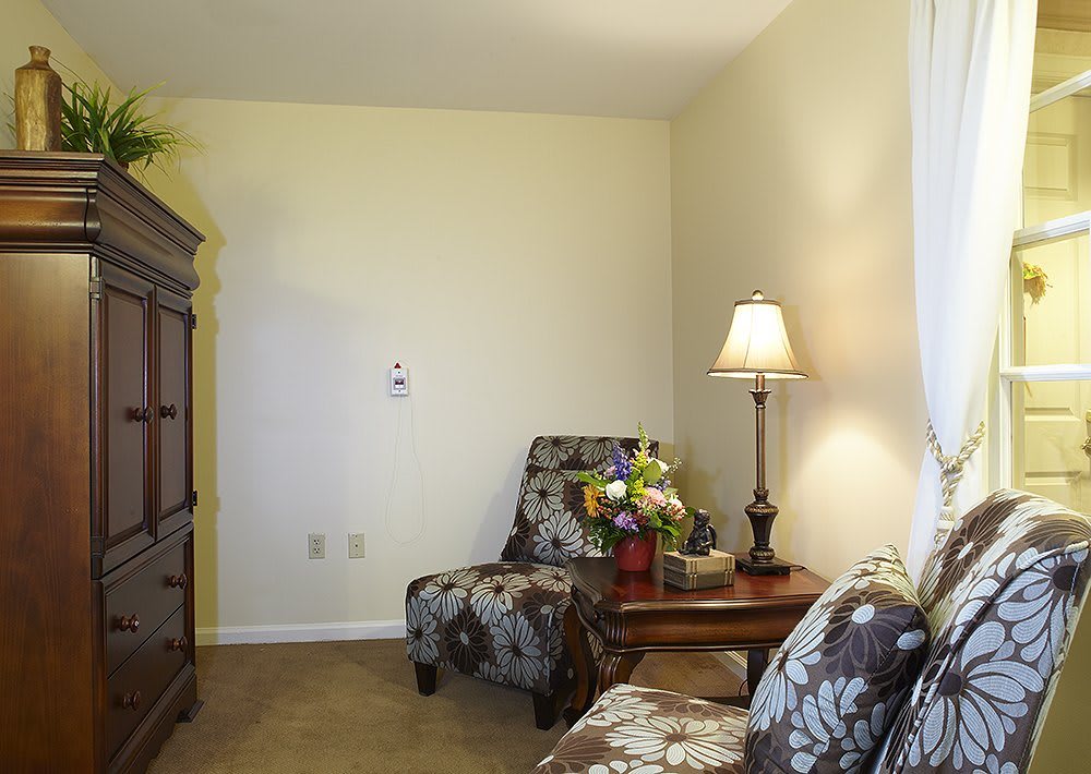 A cozy living room corner featuring floral armchairs, a side table with a lamp, and a vase of flowers.
