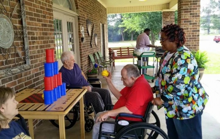 Elderly individuals in wheelchairs engaging in an outdoor activity with colorful cups.