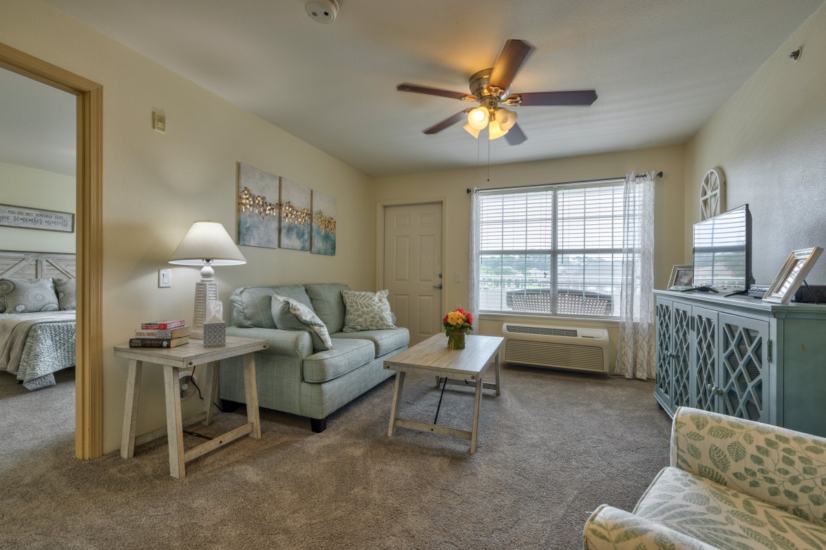 A cozy living room with a comfortable sofa, coffee table, and a warm lamp, complemented by wall art and a ceiling fan.