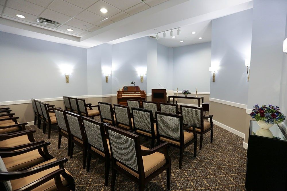 An empty chapel with rows of chairs facing an organ and altar, softly lit by wall sconces.