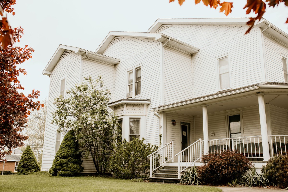 A white residential house with a porch and surrounding greenery.