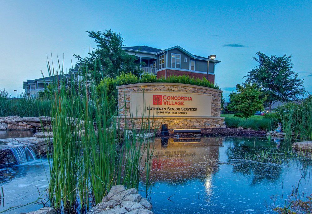 A scenic view of a building with a sign, surrounded by nature and reflected in a pond.