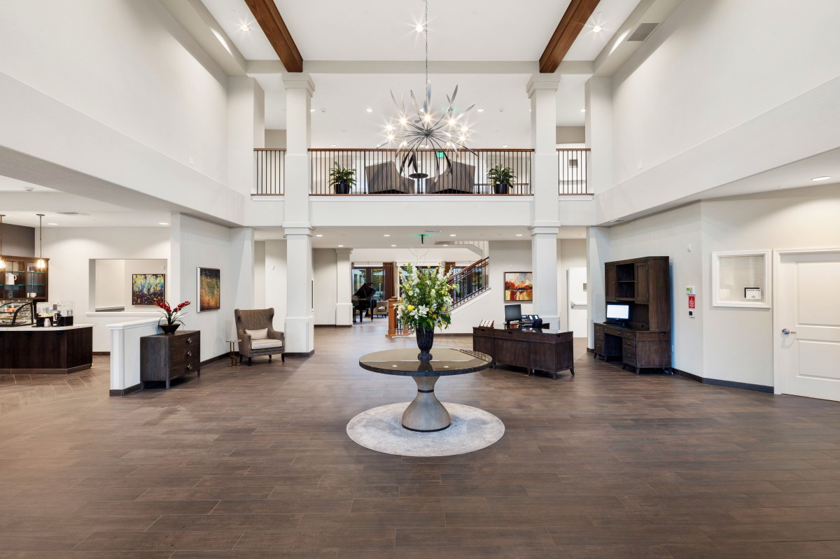 A modern and spacious lobby area featuring elegant furniture, a central table with floral decor, and a chandelier hanging from the ceiling.