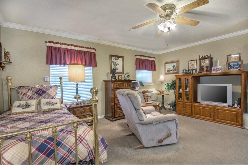 A cozy bedroom with a ceiling fan, featuring a bed, recliner, and television in a warm setting.