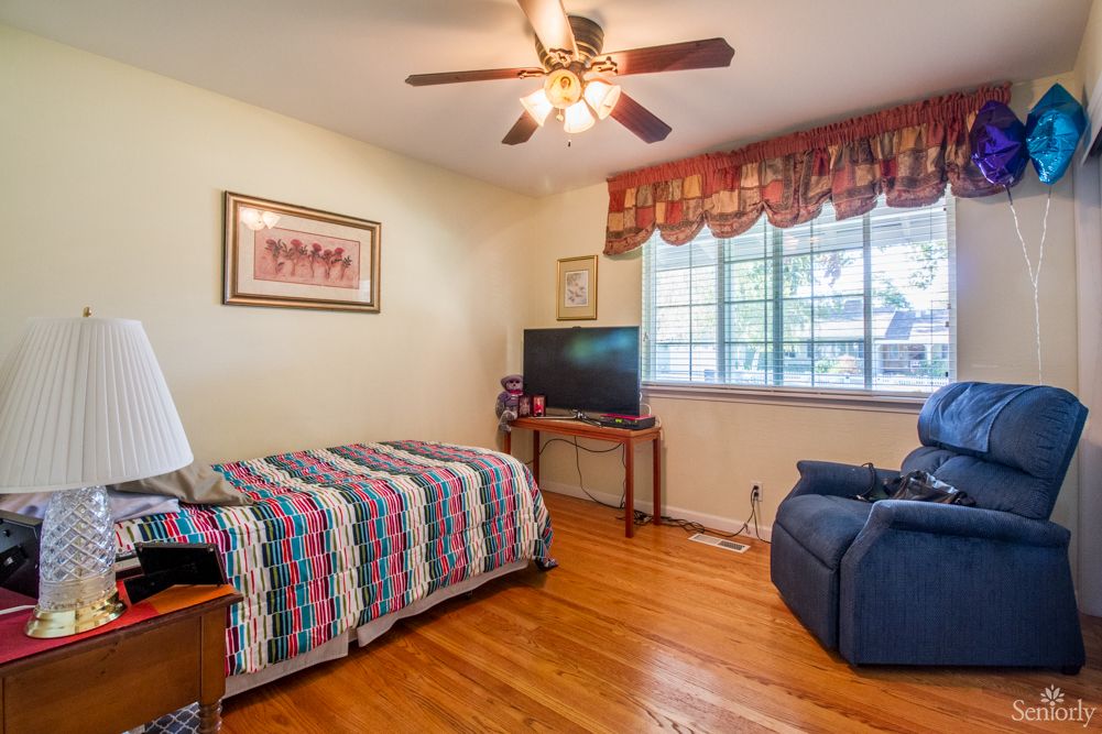 A cozy bedroom with a single bed, ceiling fan, and television.