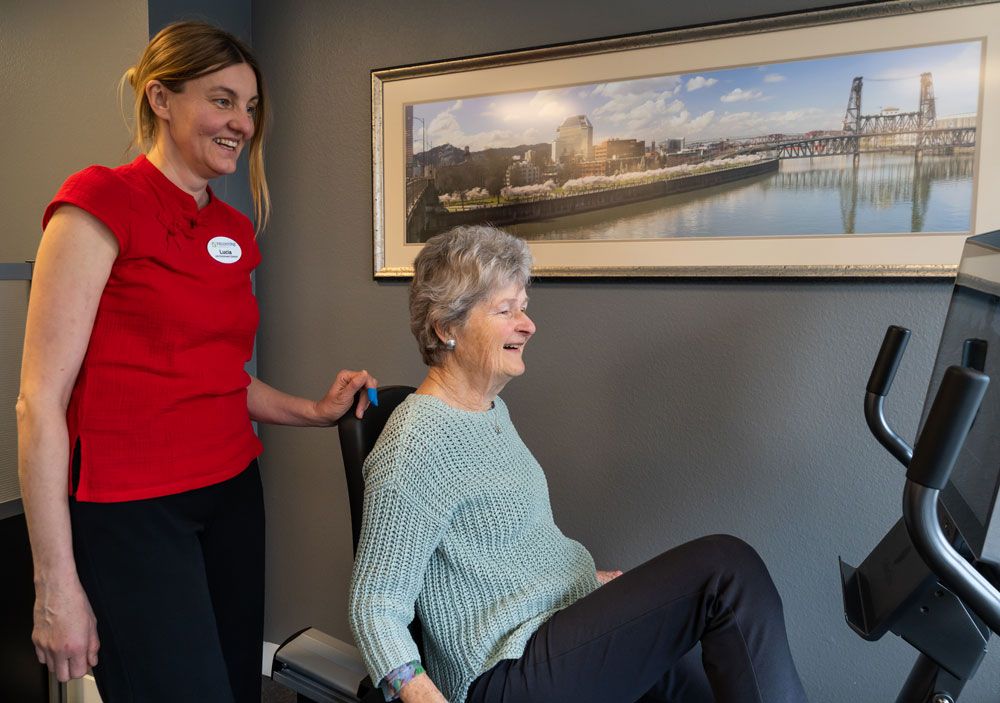 A healthcare worker assists an elderly woman with seated exercises in a comfortable setting.