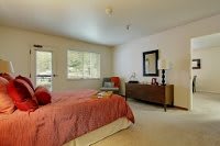 A cozy bedroom with a neatly made bed, wooden dresser, and natural light from the window.