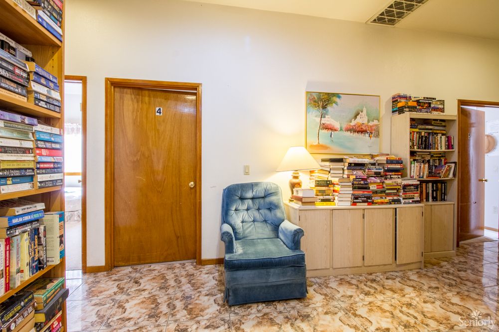 A cozy living room corner featuring a blue armchair, bookshelf, and a lamp under a painting.