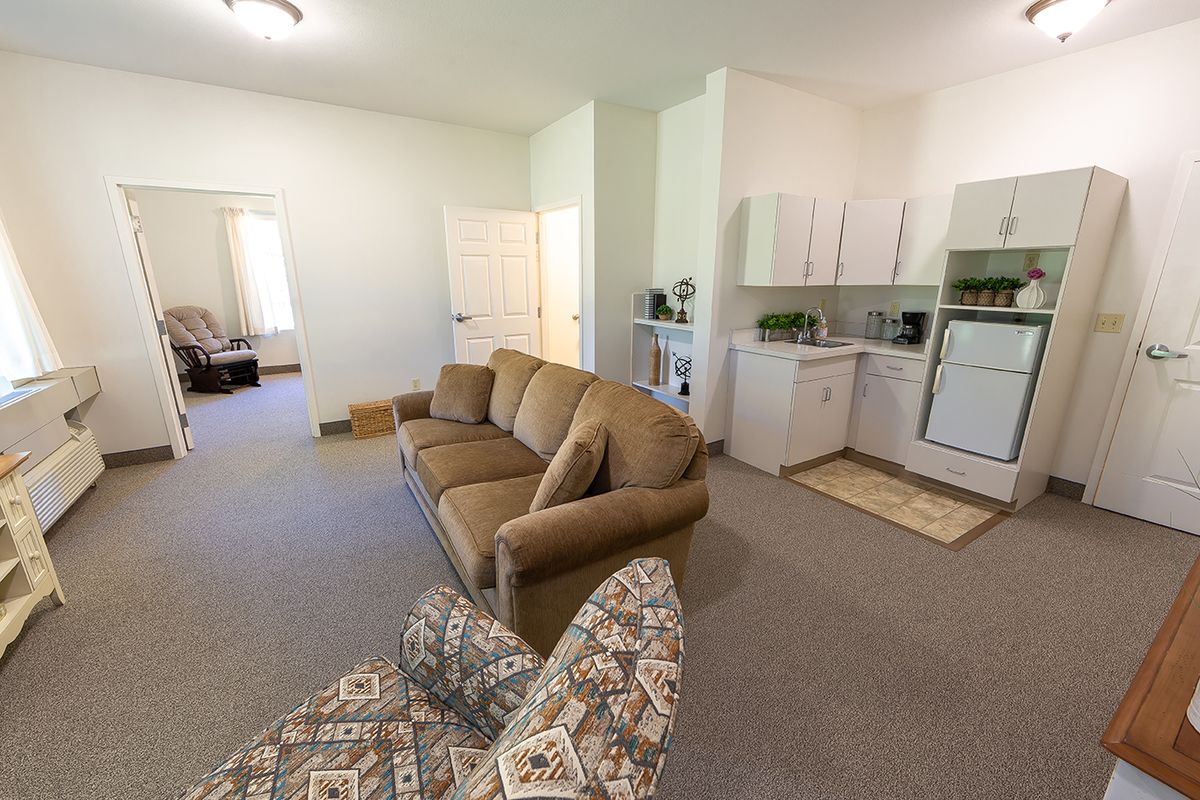 Cozy apartment interior featuring a living room with a sofa and armchair, adjacent to a compact kitchen area.