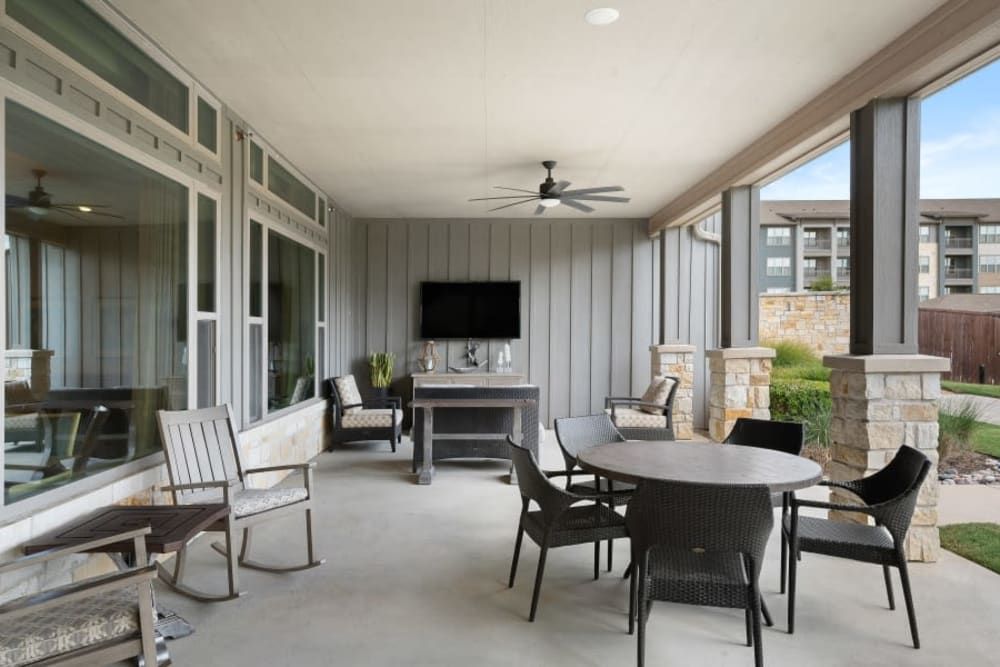 A modern outdoor patio featuring comfortable seating, a round table with chairs, a ceiling fan, and a wall-mounted TV.