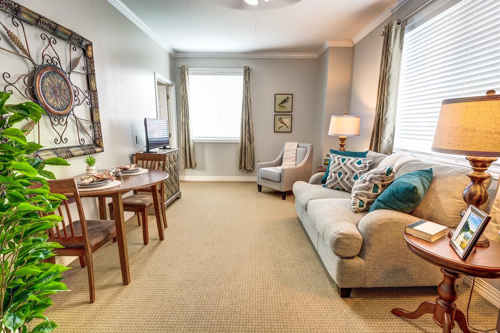 A cozy living room with a sofa, dining table, chairs, and a lamp, featuring soft lighting and decorative elements.