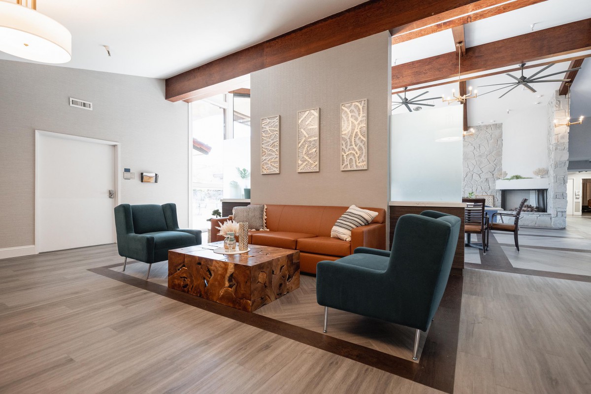 A modern living room with stylish furniture, including a brown sofa and two dark chairs around a wooden coffee table, featuring decorative wall art and wood beam accents.