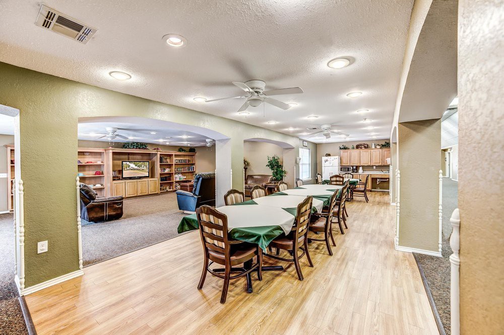 A spacious dining area with tables and chairs in an open layout, featuring a wooden floor and ceiling fans.