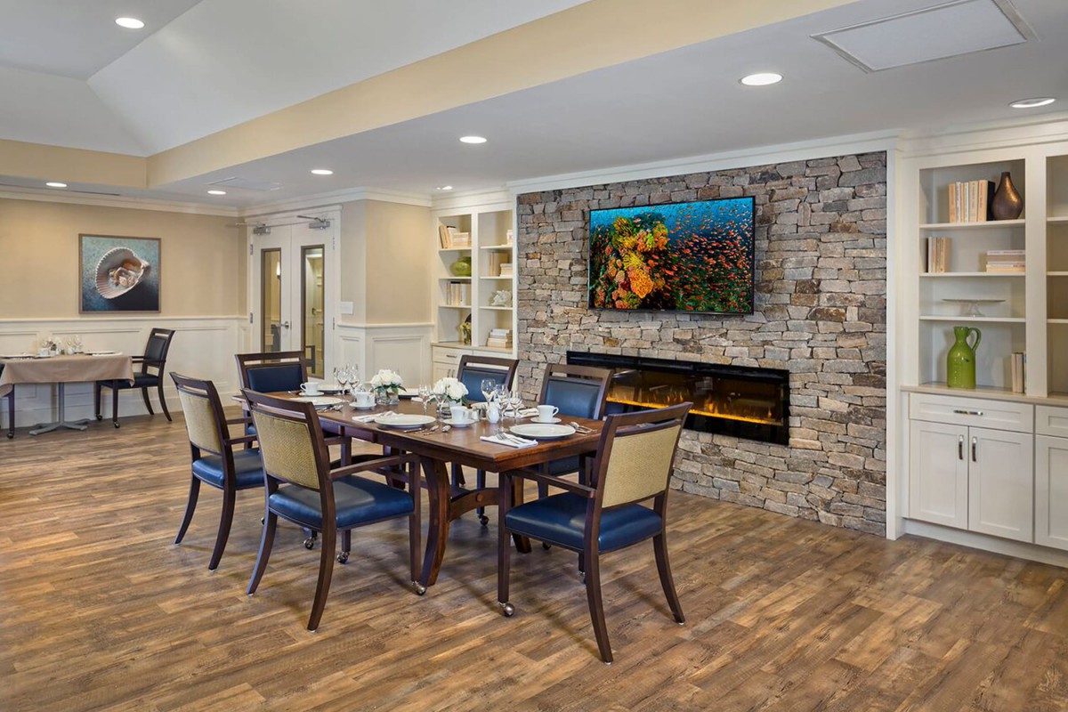Elegant dining room with a stone fireplace and artwork above, featuring a wooden table set for six.