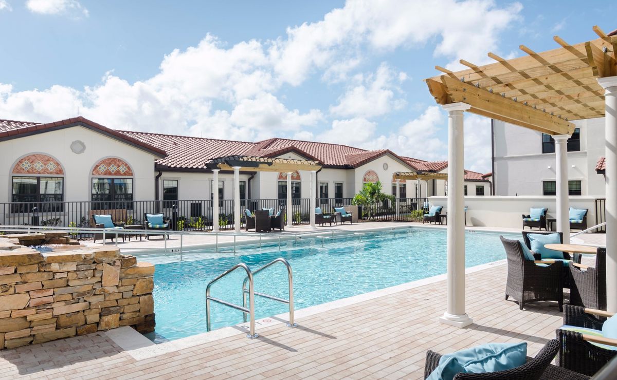 A sunny day at a residential outdoor swimming pool with adjacent patio seating and modern architecture.