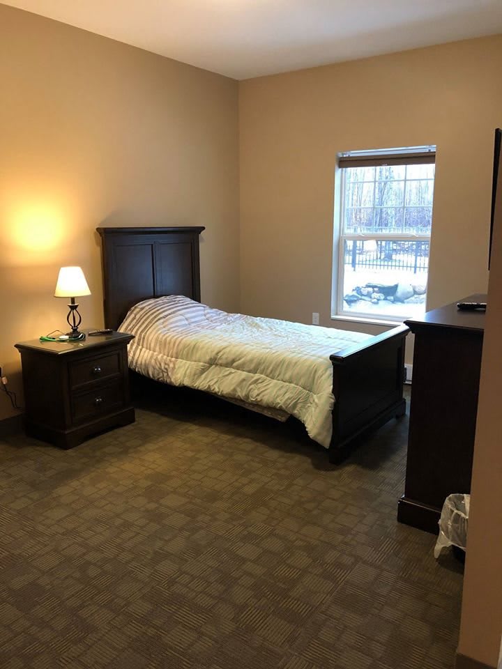 A cozy bedroom with a single bed, nightstand, lamp, and window.