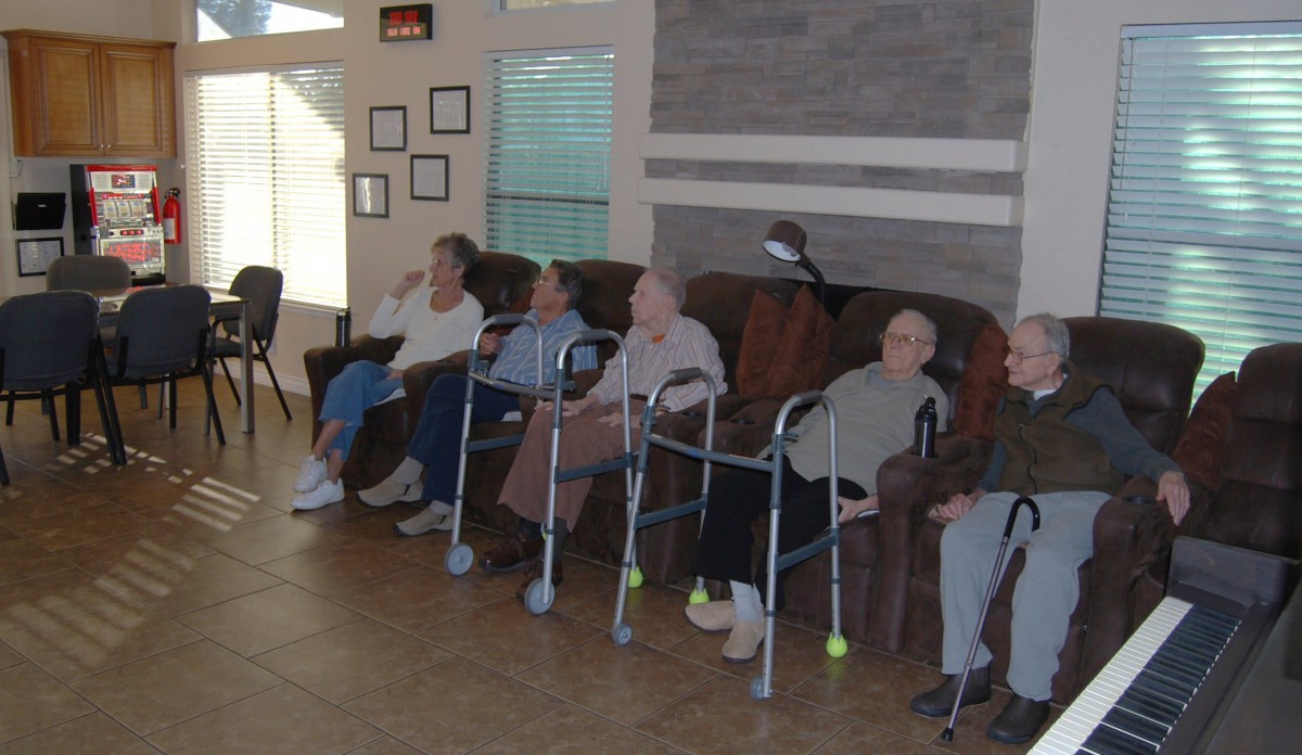 A group of elderly individuals seated indoors, some with walkers, in a community setting.