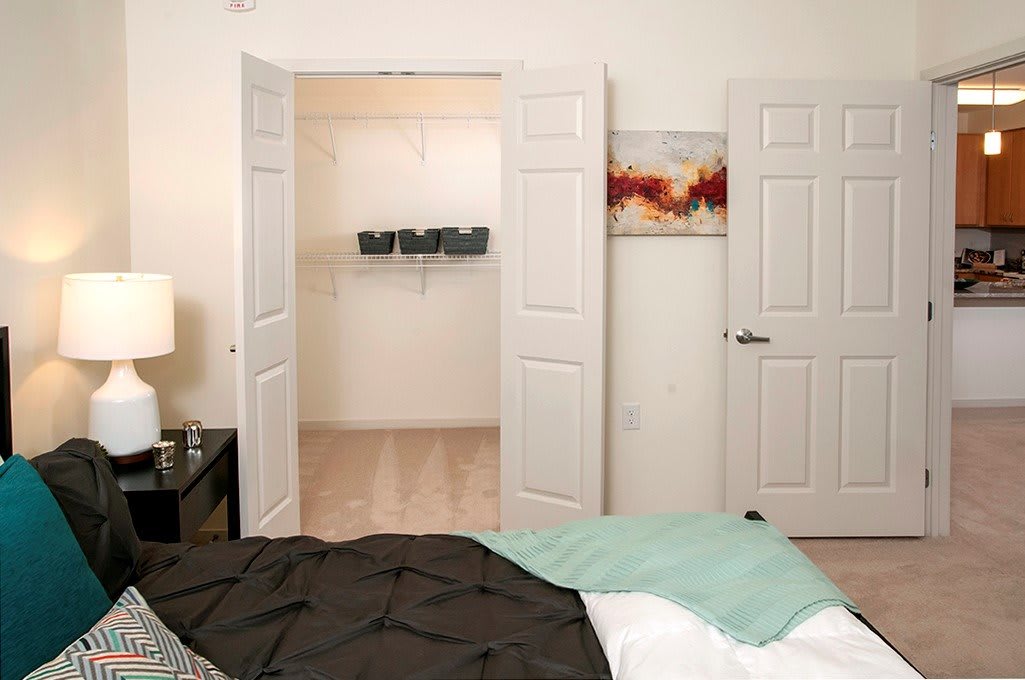 A minimalist bedroom featuring an open closet with double doors, a neatly made bed, and simple decor.