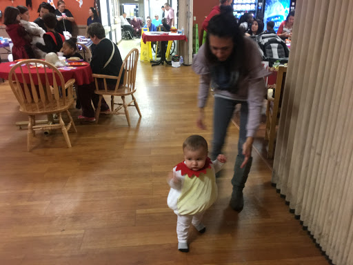 A child playfully waddles along as an adult assists in a lively dining environment.