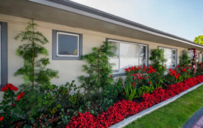 A house with a well-maintained garden featuring red flowers and green shrubs.
