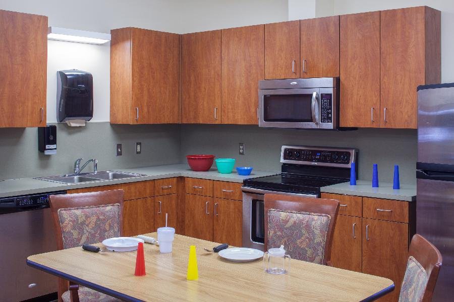A kitchen setup with a dining table, wooden cabinets, modern appliances, and various dining accessories.