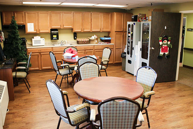 A cozy break room with tables, chairs, a vending machine, and kitchen amenities.