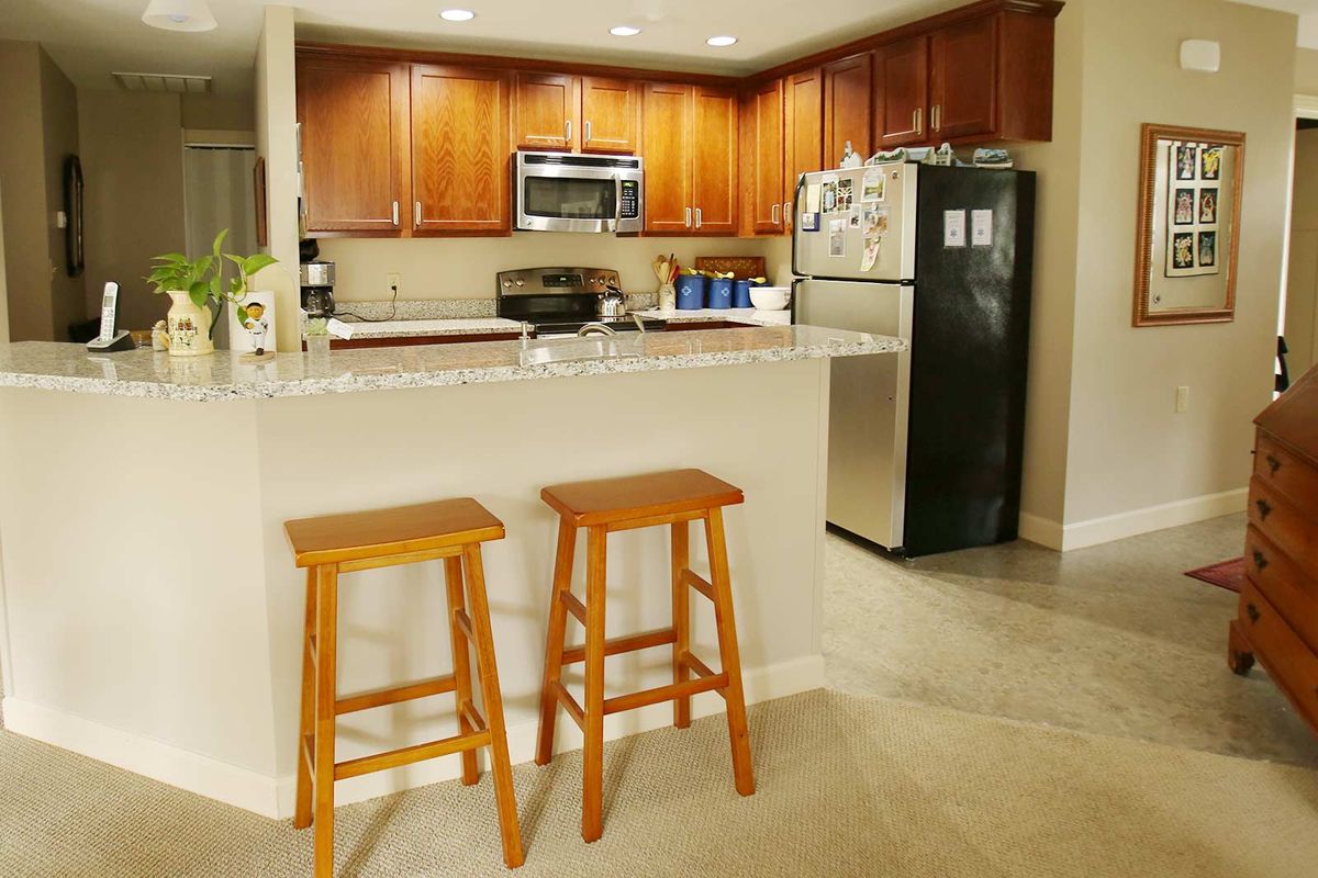A modern kitchen with wooden cabinets, stainless steel appliances, and two bar stools at a countertop.