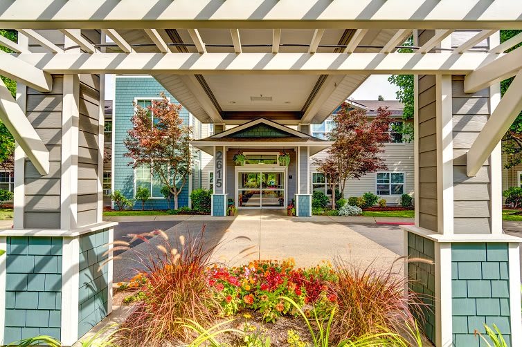 A modern building entrance with a covered walkway and vibrant landscaping.
