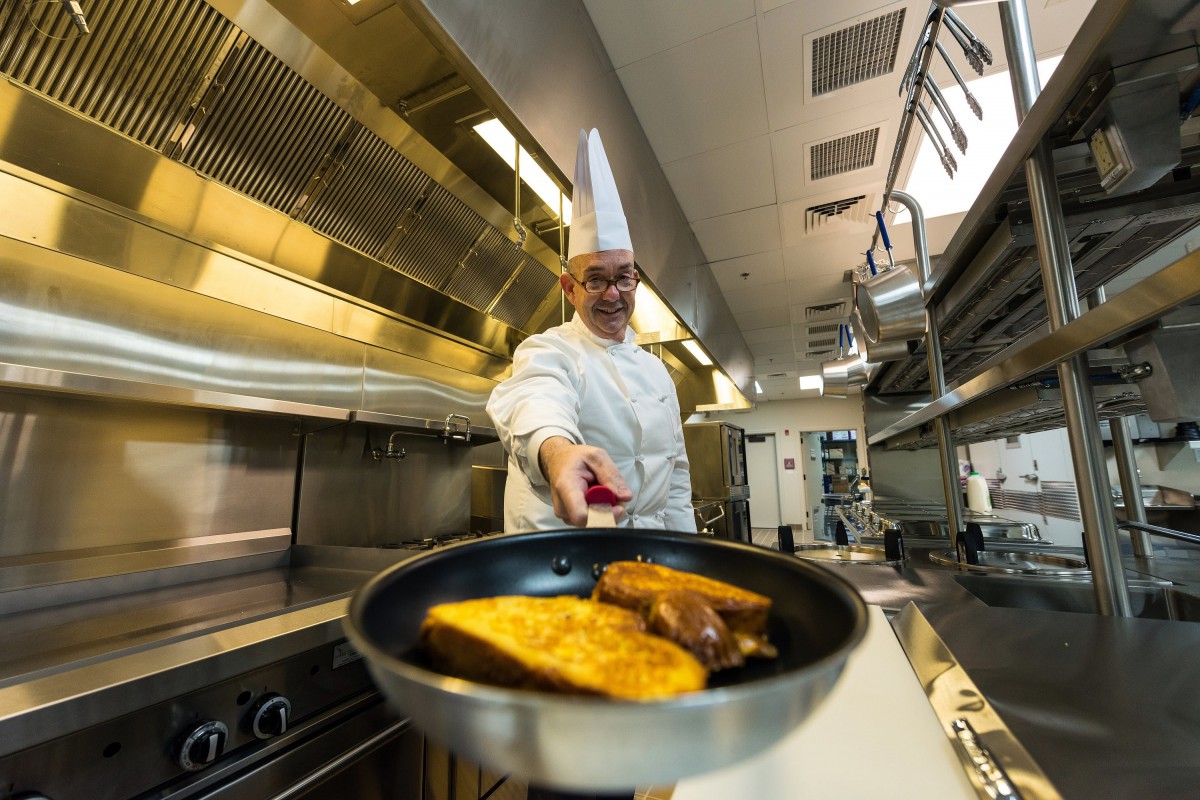A professional chef cooking in a modern kitchen, preparing toast in a frying pan.