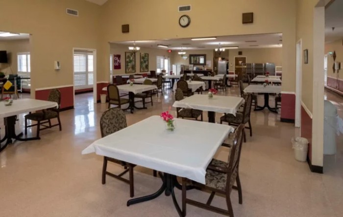 An empty dining hall with tables and chairs neatly arranged, featuring floral centerpieces.
