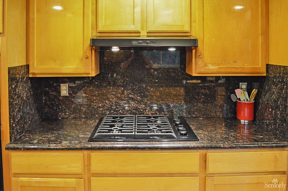 A kitchen with a gas stovetop, wooden cabinets, and a granite backsplash.