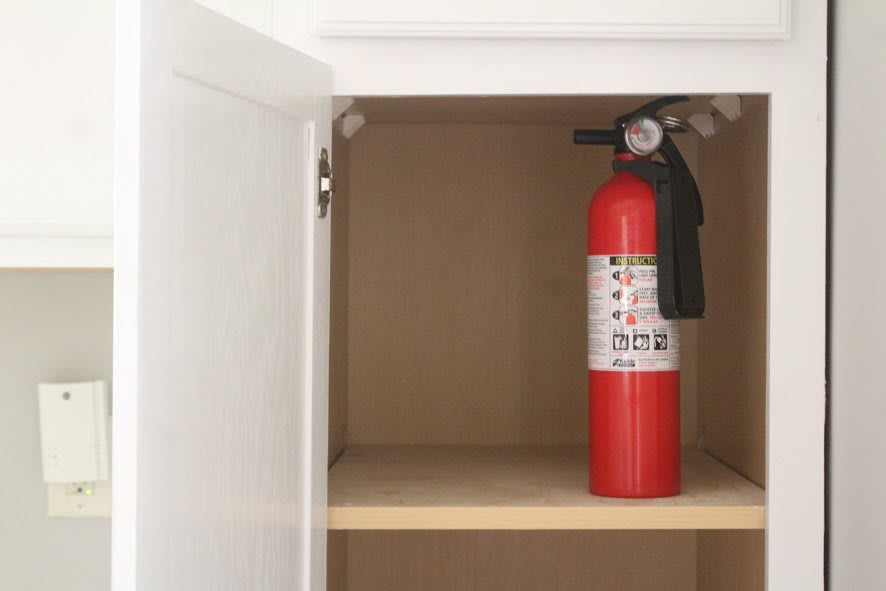 A fire extinguisher stored in a kitchen cabinet for emergency use.
