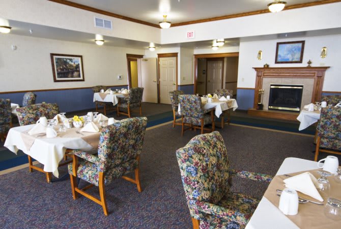 A cozy dining room with tables set for guests and a warm fireplace.
