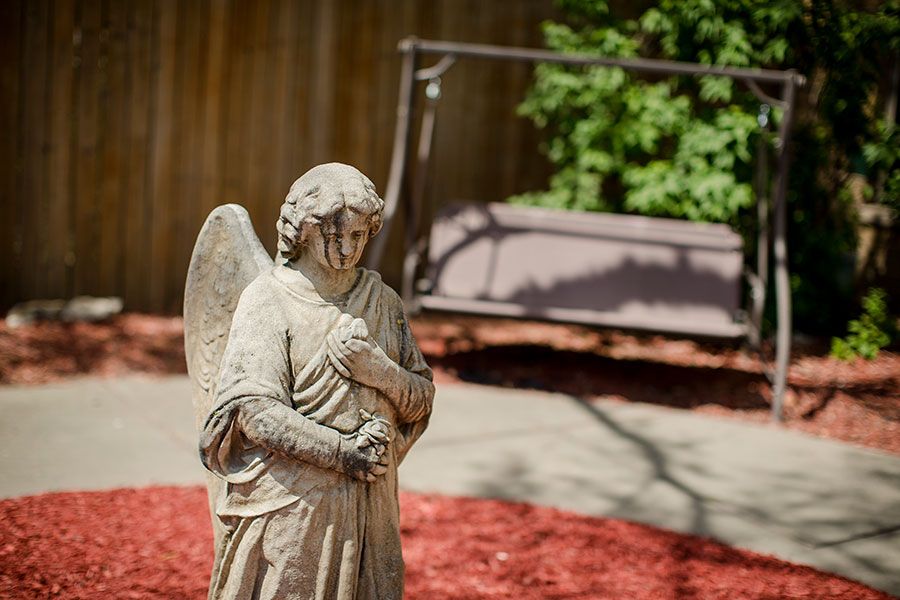 A stone angel statue stands in a garden with a swing in the background.
