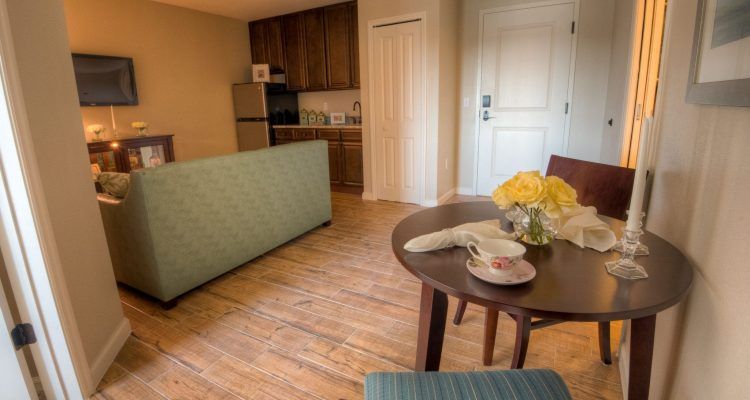 A cozy living area with a sofa, table set with flowers and a cup, and a small kitchen space.