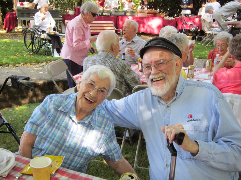 Two seniors smiling and enjoying an outdoor community picnic.