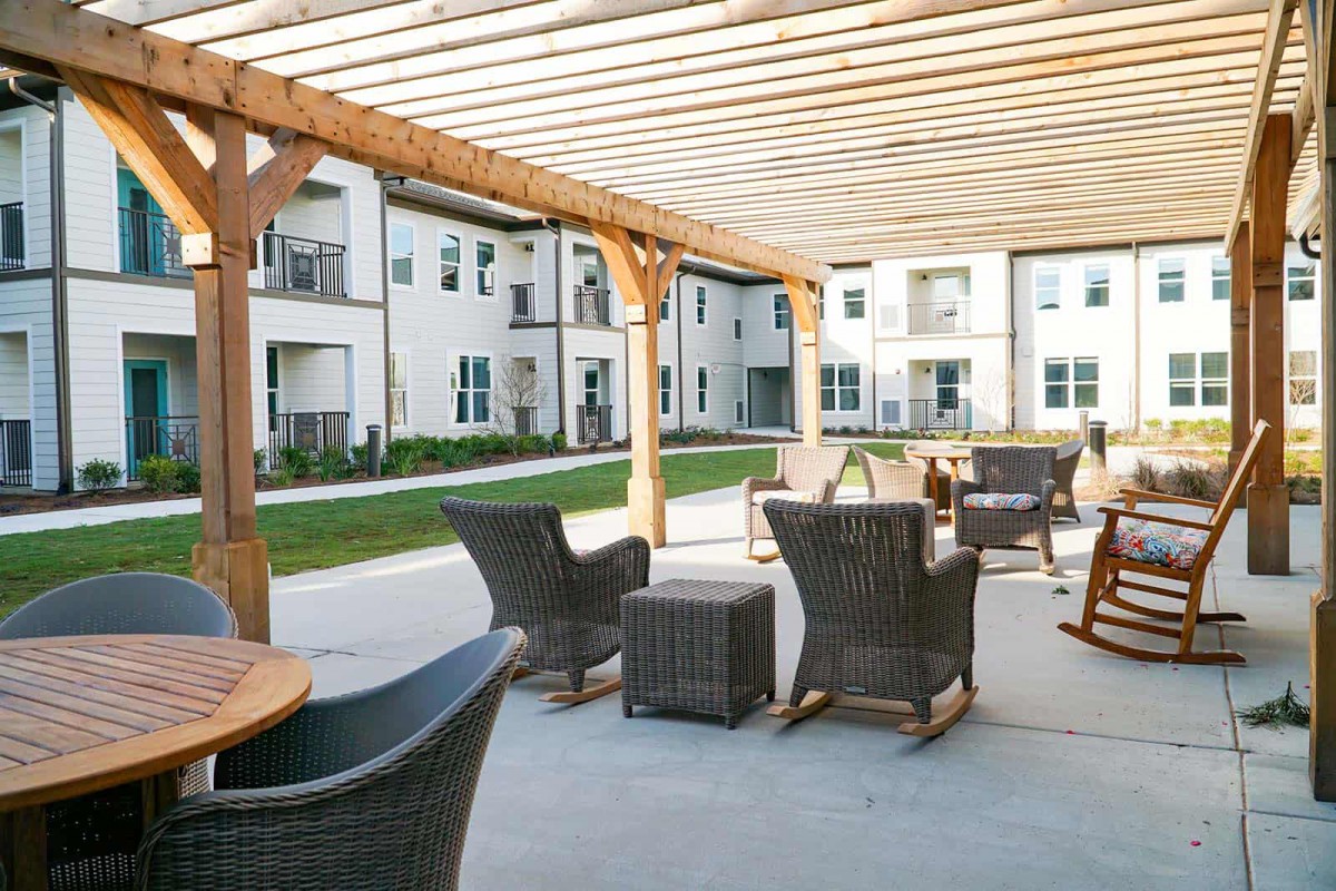 A comfortable outdoor seating area with wicker furniture under a pergola in a residential apartment complex.
