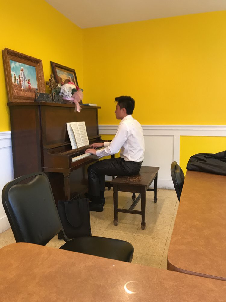 A person in formal attire playing the piano in a room with yellow walls.