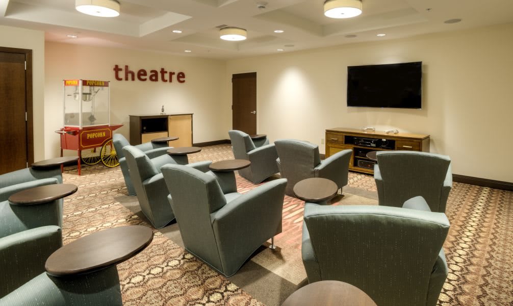 A cozy theater room with comfortable armchairs and a large television on the wall.