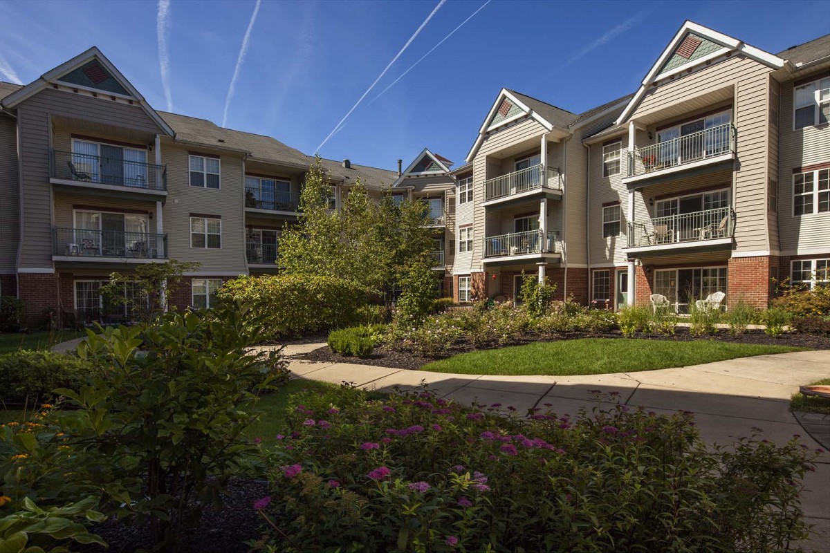 A modern apartment complex with well-maintained gardens and pathways under a clear blue sky.