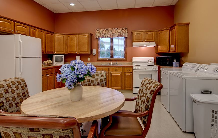 A cozy kitchen and dining area with wood cabinets, a round table adorned with flowers, and various appliances.