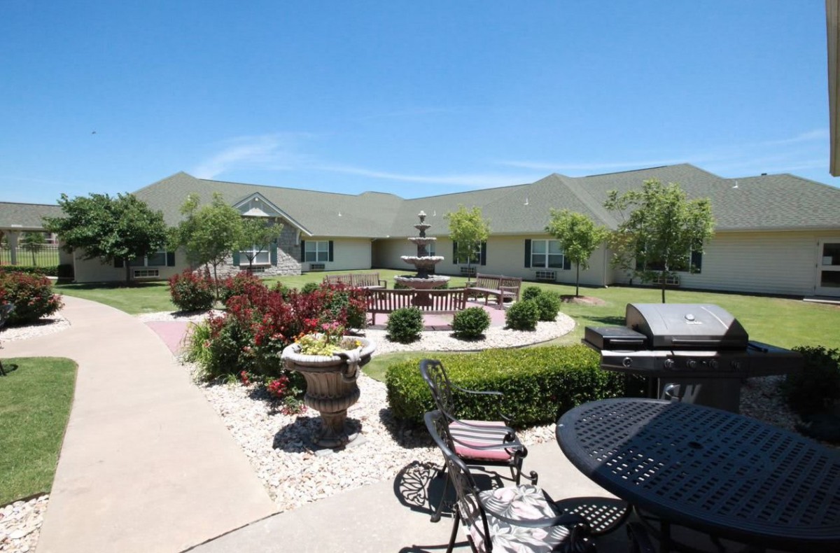 A well-maintained garden with outdoor seating and a building in the background, under a clear blue sky.