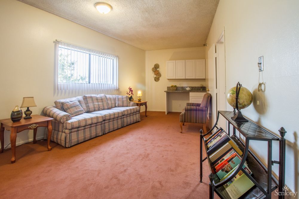 A cozy living room with a sofa, carpeted floor, and a small bookshelf near the window.