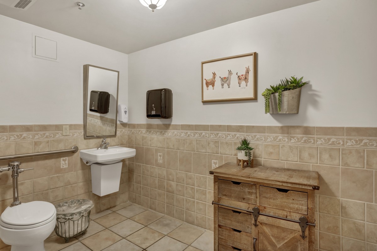 A well-decorated bathroom with a wooden cabinet, wall-mounted sink, artwork, and plants.